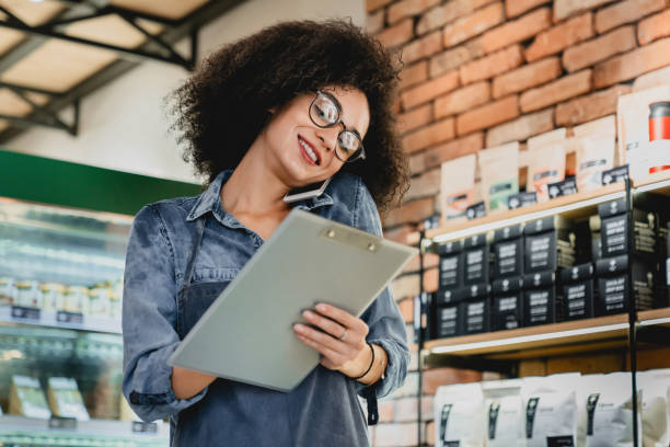 istock Qualified young good-looking barista talking by phone while writing in folder in cafeteria 1292406797