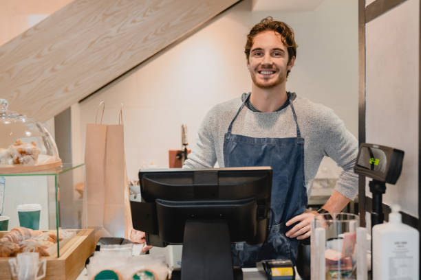 Young smiling nice-looking waiter working at the cash point in a cafe