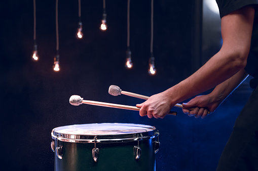 The percussionist plays with sticks on the floor tom in a dark room with beautiful lighting. Concert and performance concept.