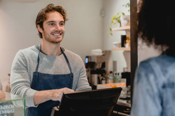 istock Smiling helpful young waiter servicing the customer at cash point in cafe 1292407208
