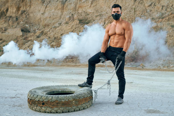 istock Bodybuilder with naked torso standing near tyre at sand pit 1292407817
