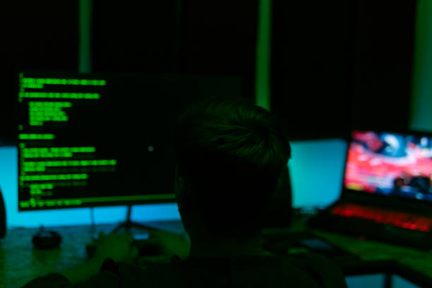 istock Hacker man looks at the screen. There are green texts on the black screen. Hacker writes code. People silhouette is looking at the screen. 1292408508