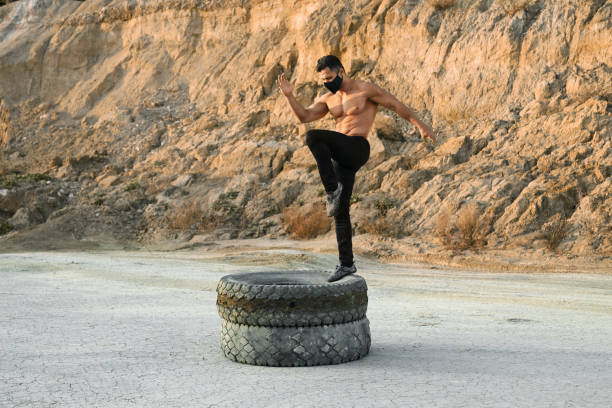Athletic man in face mask training legs on tyres
