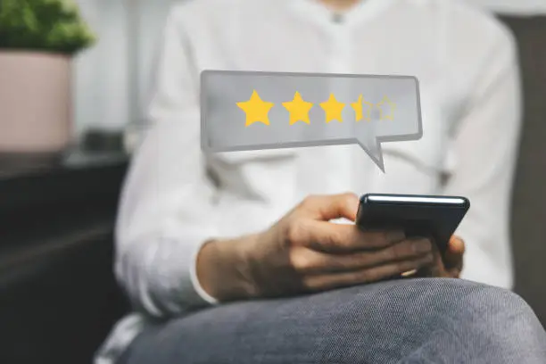 Photo of customer review - woman using phone to give feedback and rate her experience with stars about service or product quality