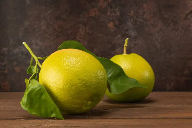 horizontal view in foreground of two grapefruits with leaves on a wooden table