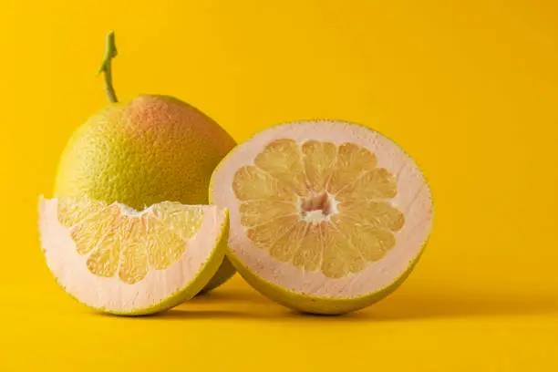 horizontal view in foreground of a half grapefruit grapefruit and grapefruit slice isolated on yellow background