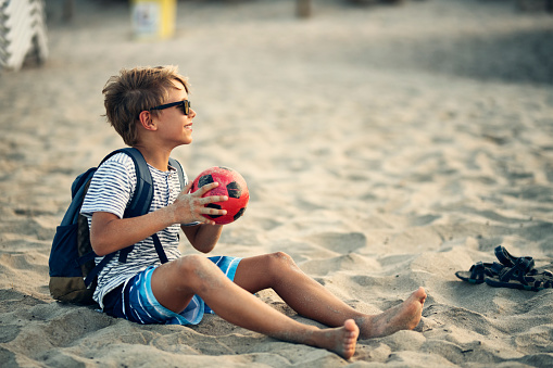 Little boy playing soccer on beach. The boy aged 9 is holding the ball and laughing at the camera.
Nikon D850