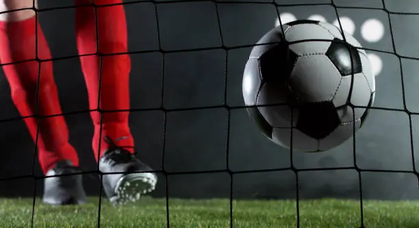 Kicking soccer ball into net, goal success concept. Isolated on black background