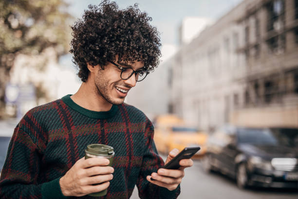 istock Handsome hipster man drinking coffee to go and using smart phone in the city 1292431103