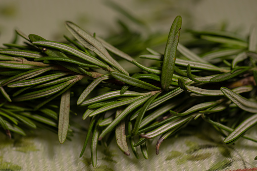 Green rosemary leaves with small seeds on cutting board in kitchen