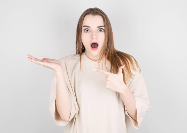 istock Happy young woman standing isolated over white wall background. Looking camera showing copyspace pointing. 1292433199