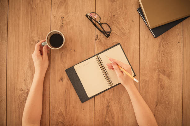 istock Human hands writing in notebook and holding a cup of coffee 1292439077