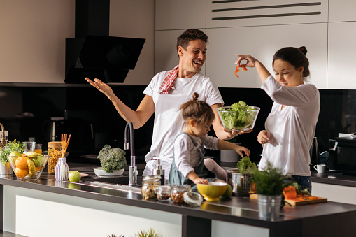 Cheerful Caucasian family with their little daughter, having fun in the kitchen, preparing a healthy food together