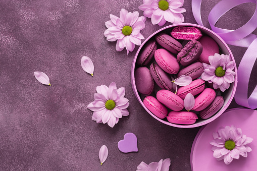Purple macaroons in a pink box decorated with flowers. Valentine's Day. View from above