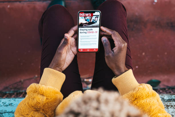 женщина читает новости о covid на мобильном телефоне - newspaper article reading the media стоковые фото и изображения