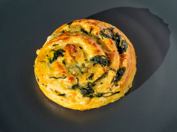 curl of dough with spinach and cheese on a dark background. Side view, close-up