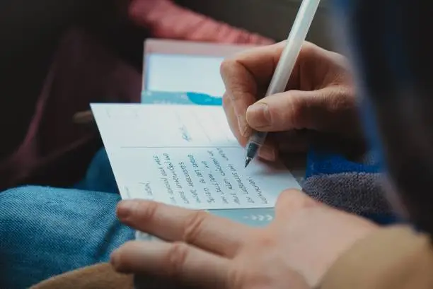 Hand of person filling in postcard with pen. Close up.