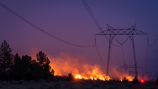 a forest fire burns under a high voltage transmission line