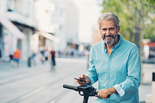 Smiling mature man with cell phone and electric scooter