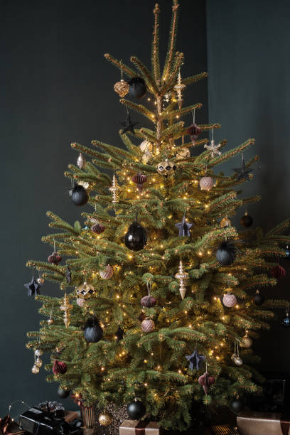istock Stylish Christmas tree on a black background. The tree is decorated with black and beige round New Year's toys. There are gifts in boxes under the tree 1292469448