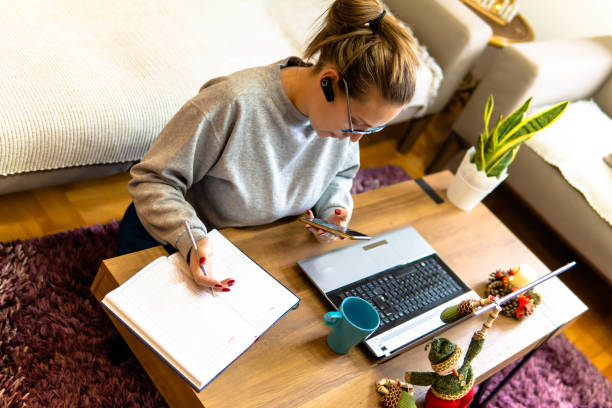 istock Remote work, office at home, work from home. Christmas time. A young woman uses a headset for an online talks, she sits on the floor with a laptop. Christmas tree and Santa. Coffee table. Earbuds 1292474205