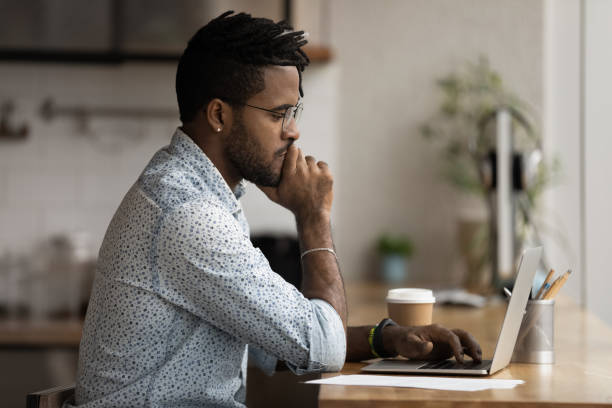 istock Pensive biracial man look at laptop screen working online 1292475534