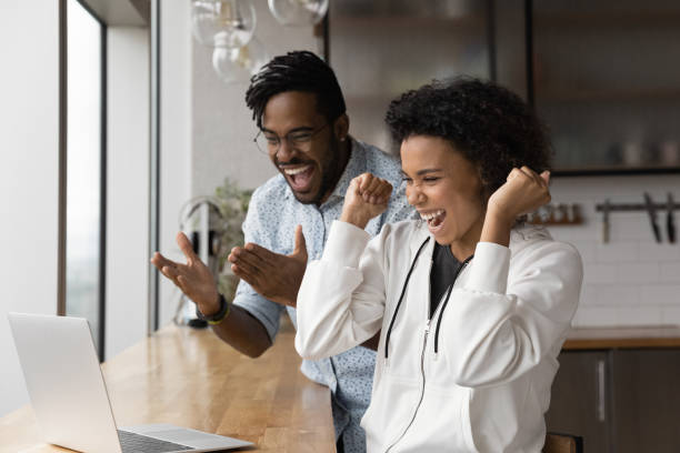 Overjoyed biracial couple celebrate lottery win on laptop Overjoyed African American man and woman feel euphoric winning online lottery on laptop. Happy excited young biracial couple winner triumph get unbelievable good news or message on computer. unusual couple stock pictures, royalty-free photos & images