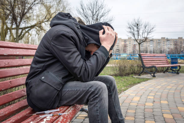 Drug abuse concept. Addict in the hood sitting on a bench in the park. Life style. Drug abuse concept. Addict in the hood sitting on a bench in the park. Life style. addiction, treatment  stock pictures, royalty-free photos & images