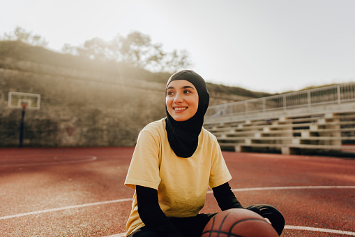 Portrait of a smiling young woman with a hijab, ready to play some basketball
