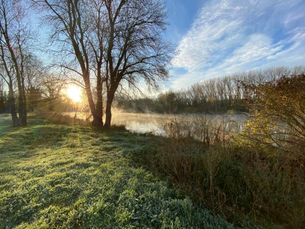 istock Sun rising on a river shore landscape with quiet waters reflecting clouds in the sky on a winter landscape 1292478493