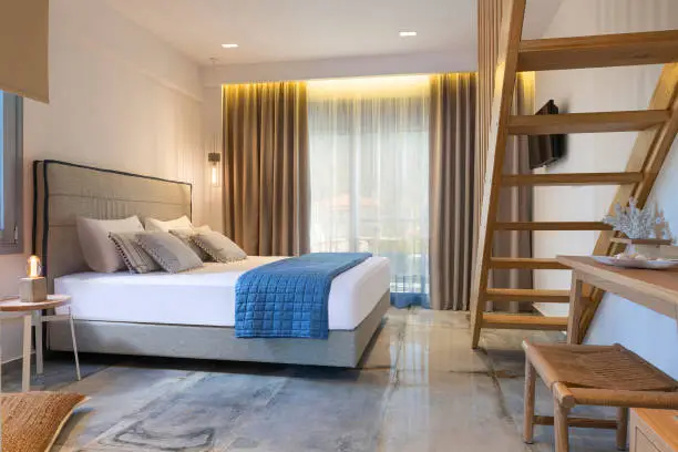 Modern nautical style interior of hotel apartment white bedroom with pine wood ladder, handmade wooden furniture, grey soft textile double bed
