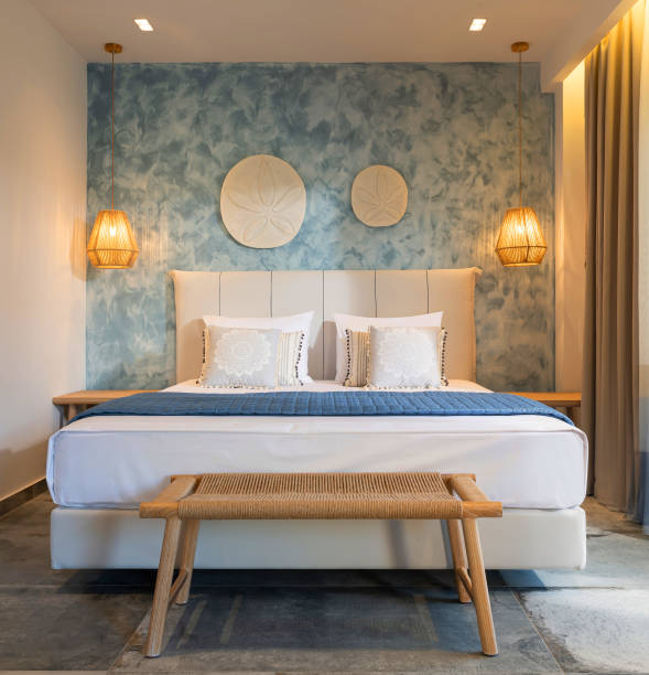 front view of modern bedroom interior in nautical marine style with blue decorative stucco wall, wicker furniture, ceiling wooden lamps, white soft bed - greece blue house wall imagens e fotografias de stock