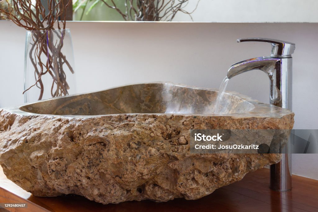 Water running into original stone washbasin Water running from bathroom tap into original stone washbasin with decoration branches on glass vase  on the side. Luxury interior design, creative concept Apartment Stock Photo