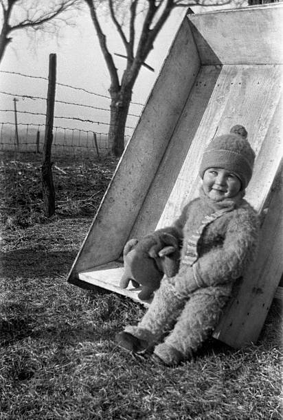 baby boy sitting in wagon bed on farm in winter 1926 Baby boy dressed in winter clothes playing with stuffed animal while sitting outdoors in wagon bed on farm in winter of 1926. Wellman, Iowa, USA. 1926 stock pictures, royalty-free photos & images