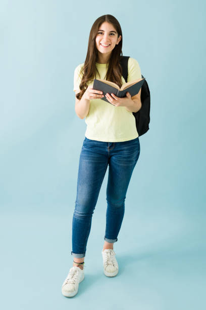 istock Portrait of a female student with a backpack standing and reading a book 1292484720