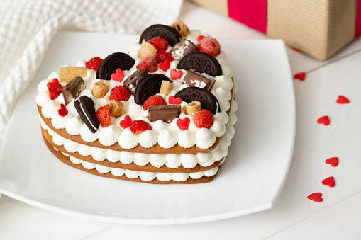 Heart-shaped cake with ricotta and whipped cream, garnished with chocolate, waffles, cookies and strawberries