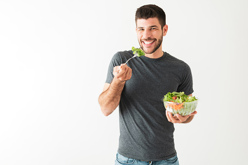 Portrait of an attractive and fitness man in his 20s eating vegetables with a fork and holding a green salad