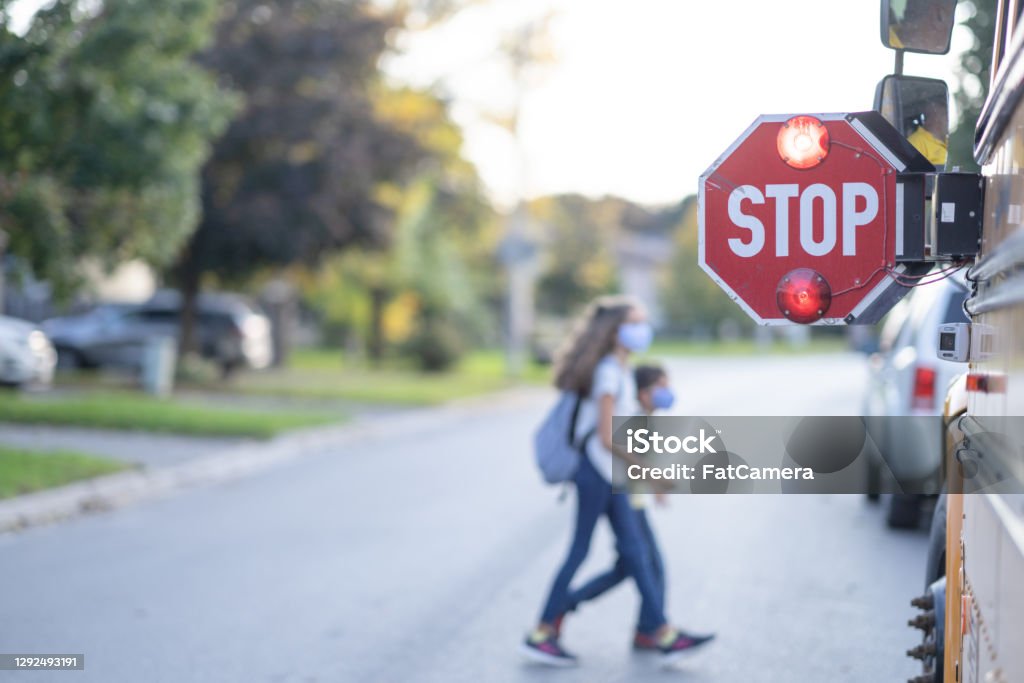 School bus stop sign for children to pass A STOP sign is out by the school bus and children can be seeing crossing the road in front of the school bus. School Bus Stock Photo