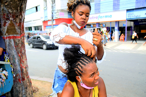 salvador, bahia, brazil - december 14, 2020: Young man is seen making afro moths on the hair of a black woman on the street in downtown Salvador.