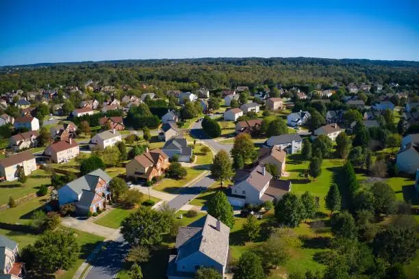 Shot using a drone during the golden hour shows an upscale suburbs with gold course, lake, houses and roof tops