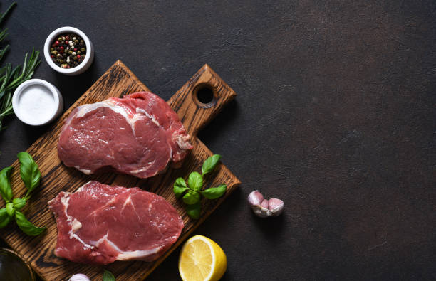 raw cooking ribeye beef steak with basil on a wooden board. view from above - top sirloin imagens e fotografias de stock