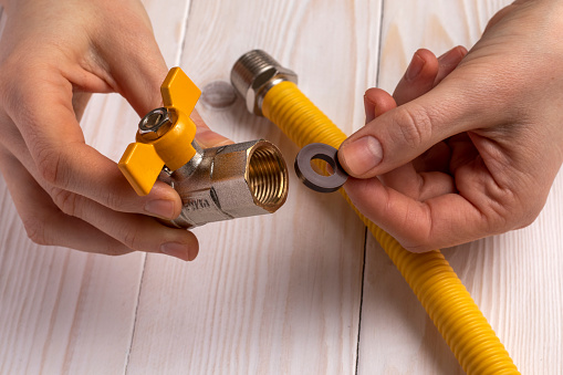 Woman plumber demonstrates a gas stopcock with internal (female) thread and a gasket. On white wooden background.