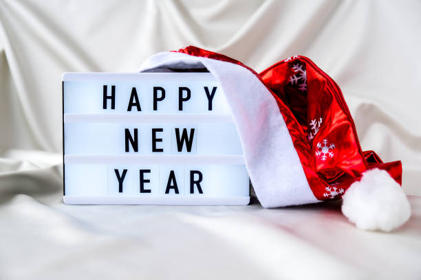 istock Lightbox with text HAPPY NEW YEAR with santa hat on silk fabric background. Winter holiday concept 1292530801