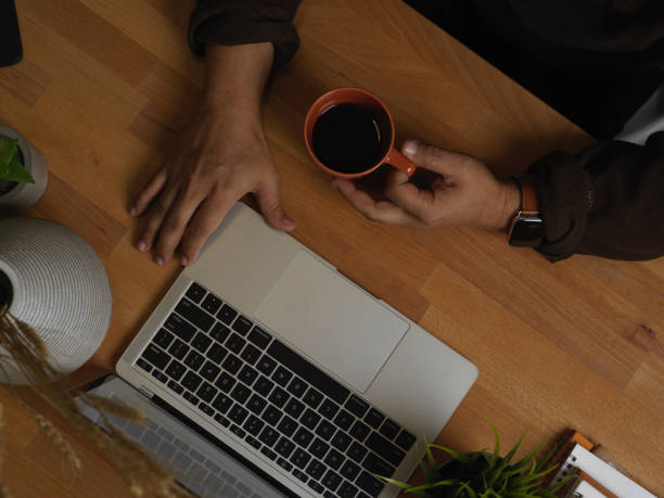 istock Male hand holding coffee cup while working with laptop in hone office room 1292531863