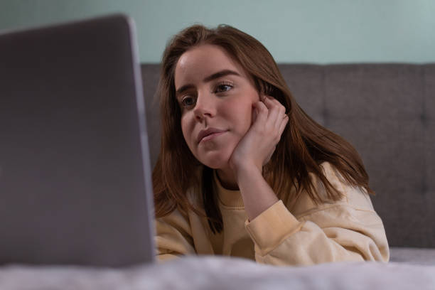 istock woman using laptop on bed with yellow sweatshirt 1292531949