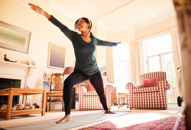 Young woman in the warrior pose during a yoga session at home Smiling young African woman practicing her warrior pose during a yoga session in her living room at home warrior position stock pictures, royalty-free photos & images