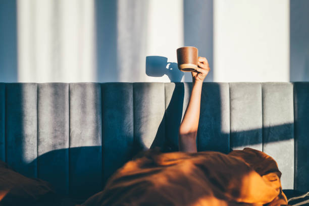 Hand holding a cup of coffee while lying on bed. Morning concept. stock photo
