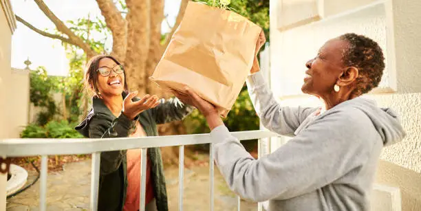 Smiling young woman delivering a bag of groceries to a senior woman outside of her home