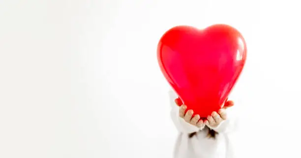 unrecognizable woman holding heart shaped ballon in front of his head, against white background in white sweater. Happy valentines day. love and relationships concept