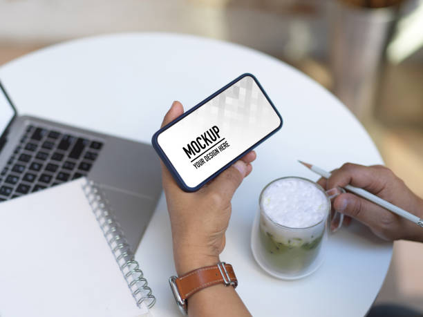 istock Male hands using horizontal smartphone on coffee table with laptop and notebook 1292537213